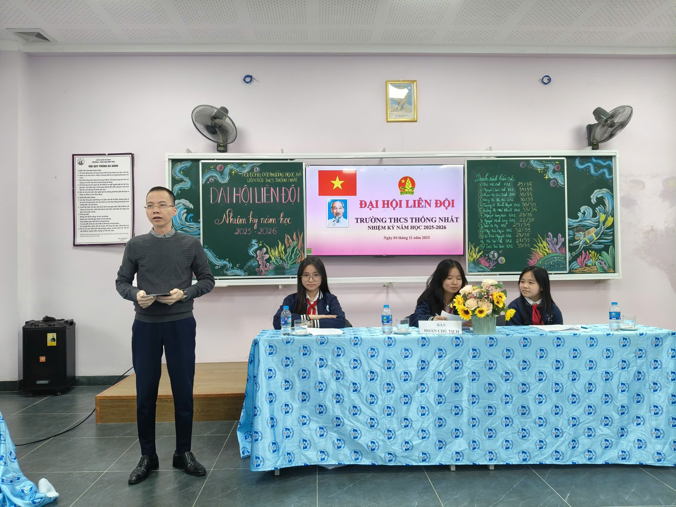 A person standing in front of a table with a group of people

Description automatically generated