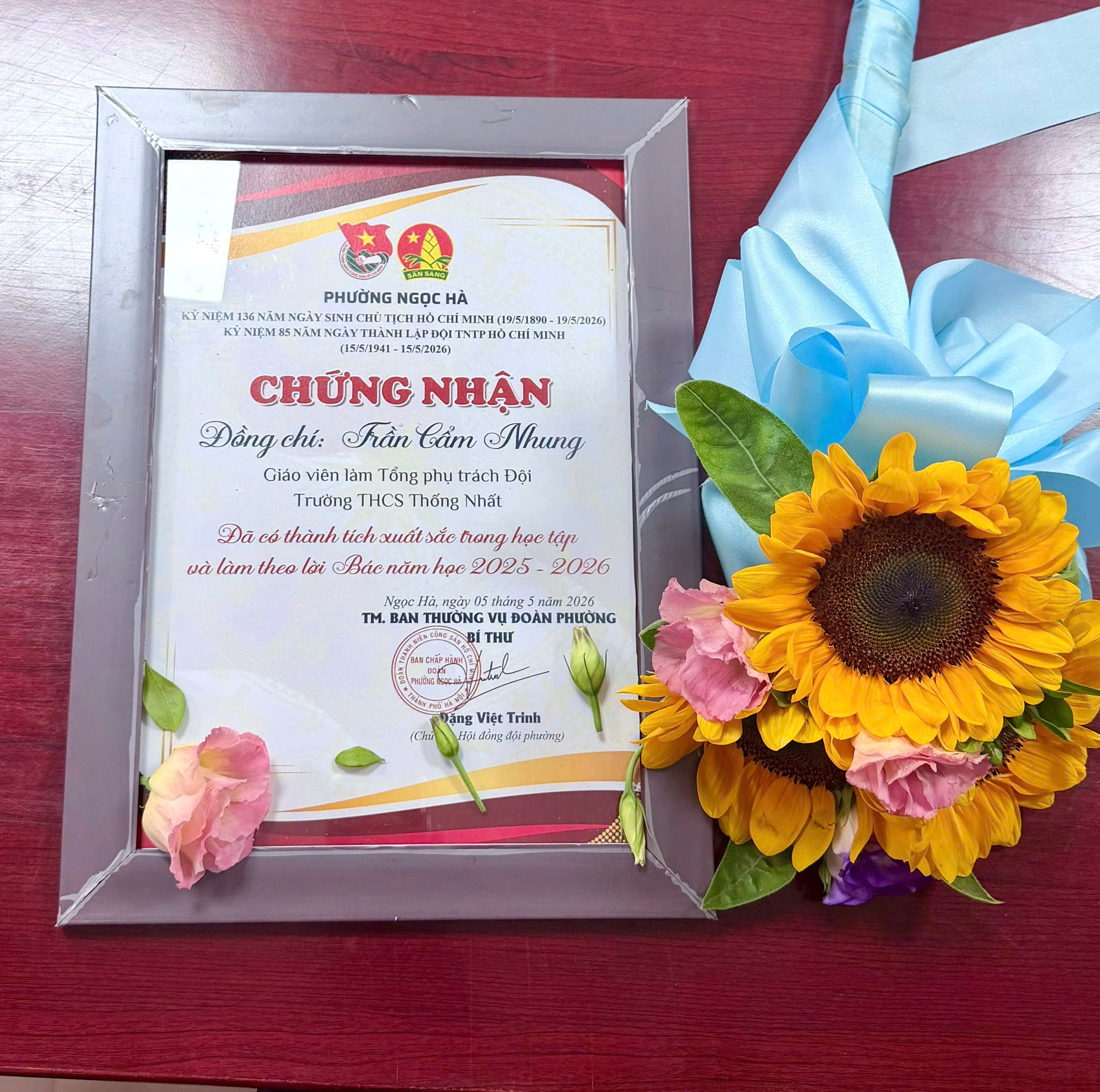 A frame with flowers and a ribbon on a red surface

Description automatically generated