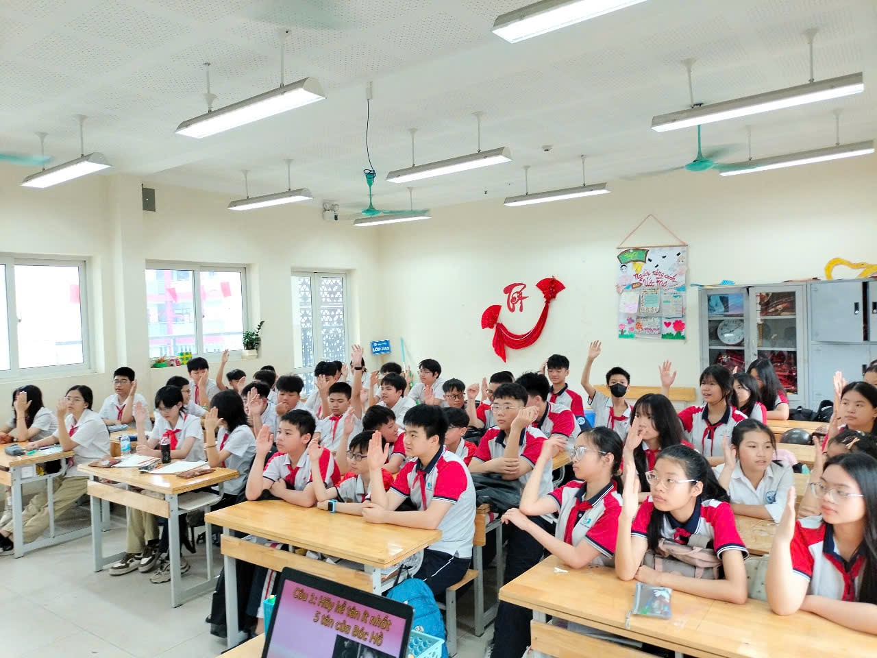 A group of students in a classroom raising their hands

Description automatically generated