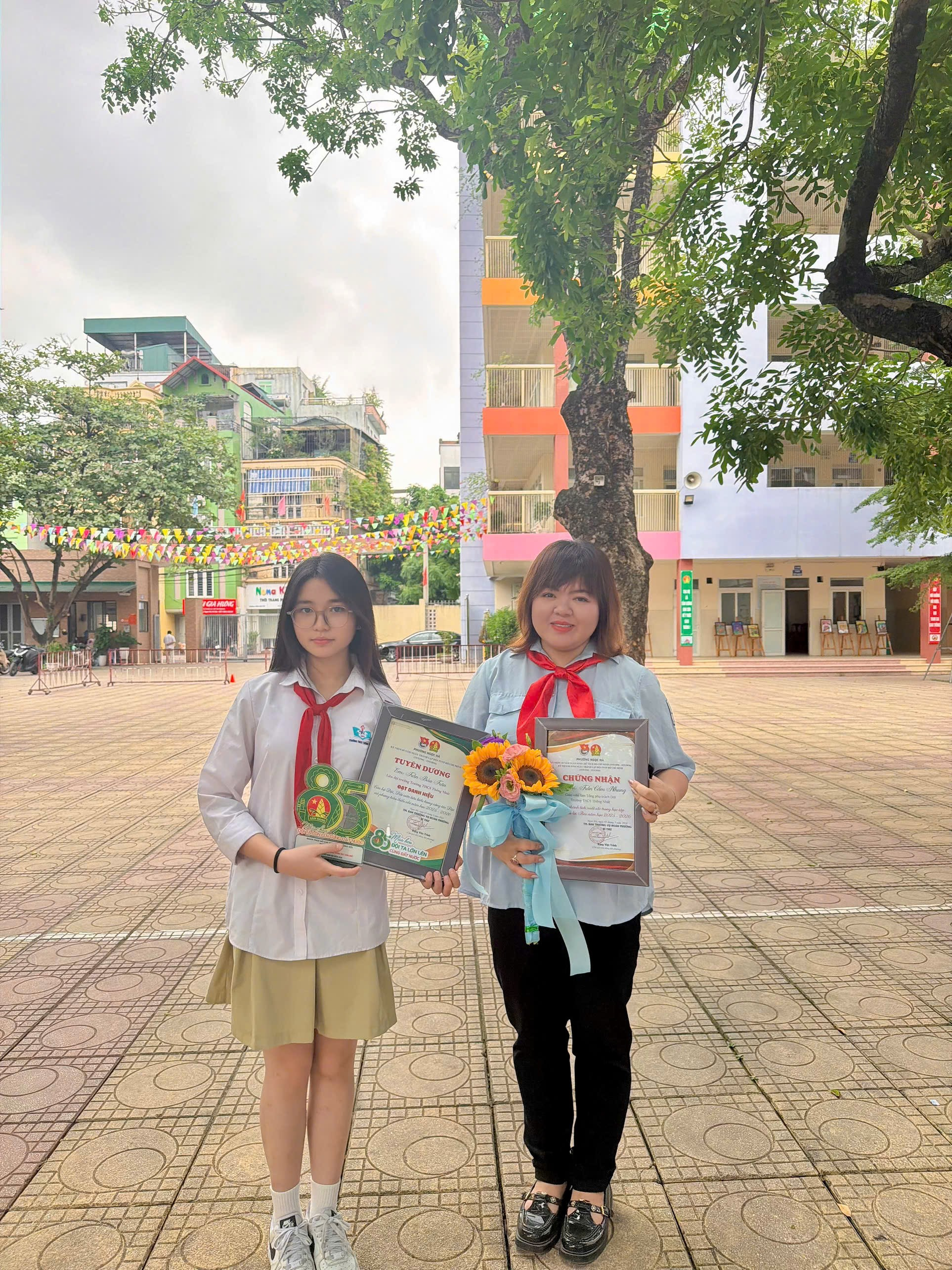 Two girls holding certificates and flowers

Description automatically generated